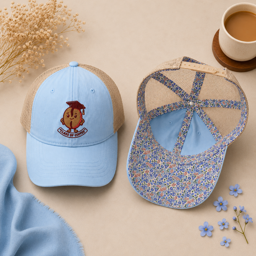 Two blue baseball caps with floral patterns on a beige surface with flowers and a cup of coffee.
