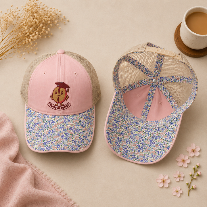 Two floral-patterned baseball caps on a beige surface with a cup of coffee and flowers.
