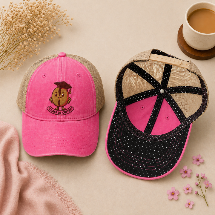 Two pink baseball caps with different designs on a beige surface with flowers and a cup of coffee.