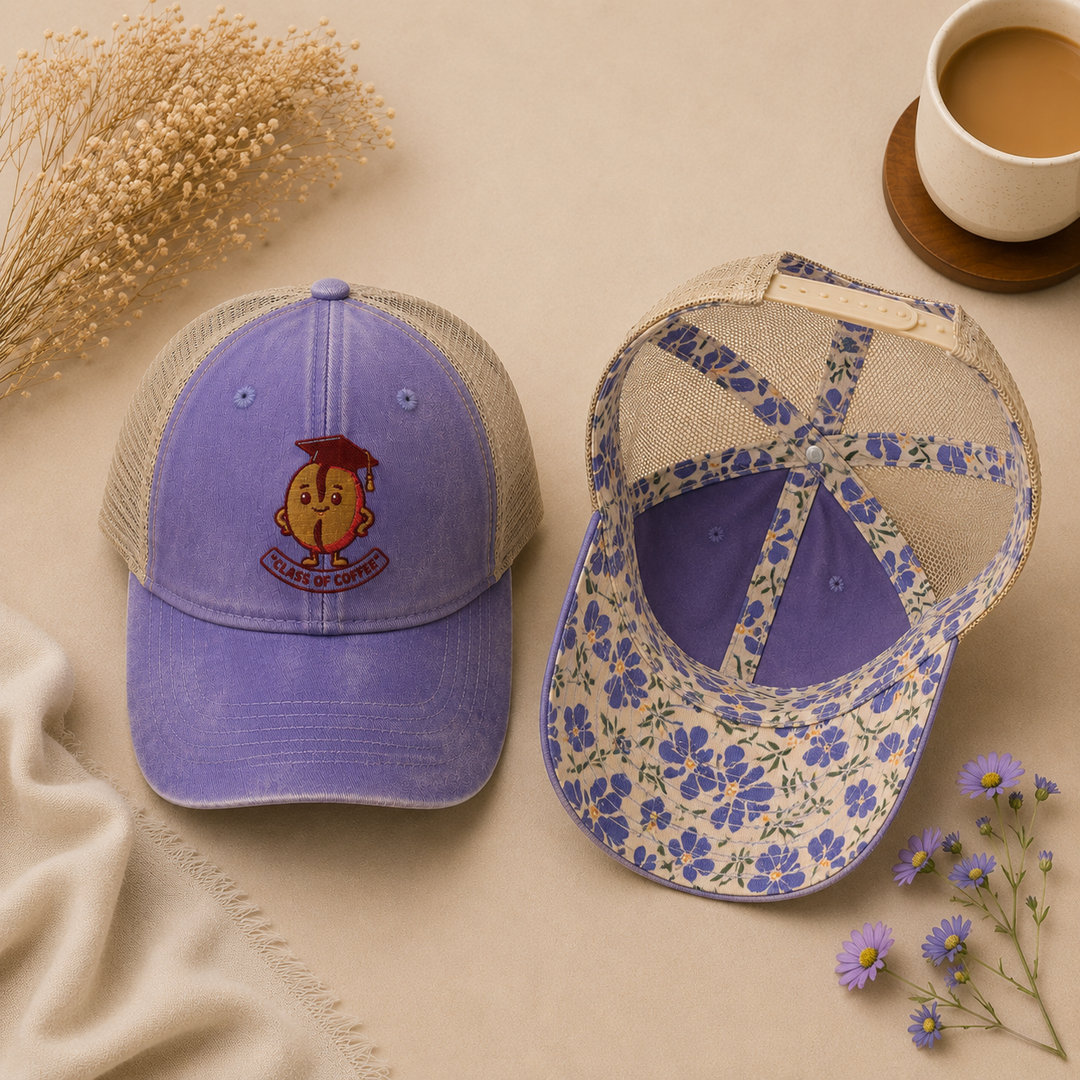 Two baseball caps on a beige surface with a cup of coffee and flowers.