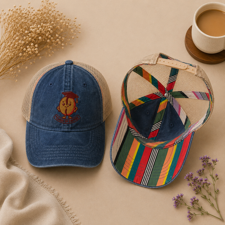 Two hats, one blue with a logo and one multicolored striped, on a beige surface with flowers and a cup of coffee.