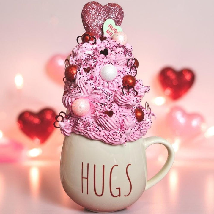Pink whipped cream dessert with heart-shaped decorations on a mug labeled &