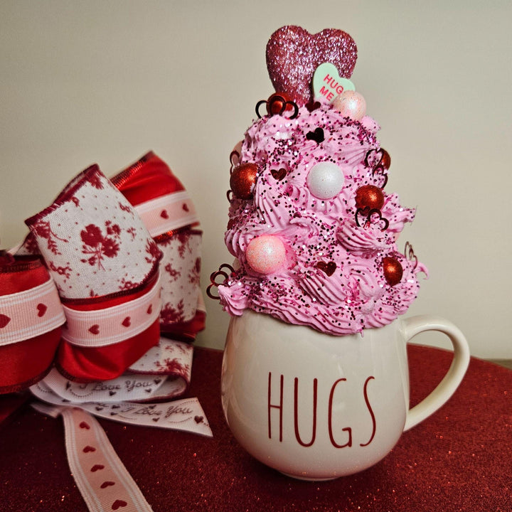 Decorative cup with pink whipped cream, heart-shaped decorations, and &