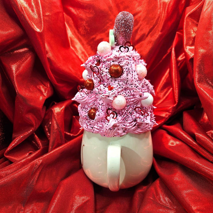 Decorative cup with pink whipped cream and chocolate pieces on a red fabric background