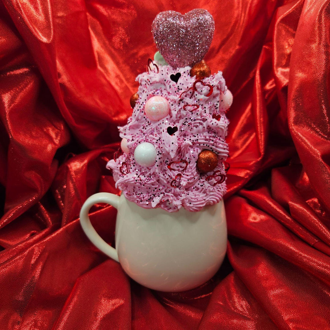 Decorative cup with pink whipped cream and heart-shaped top on a red satin background