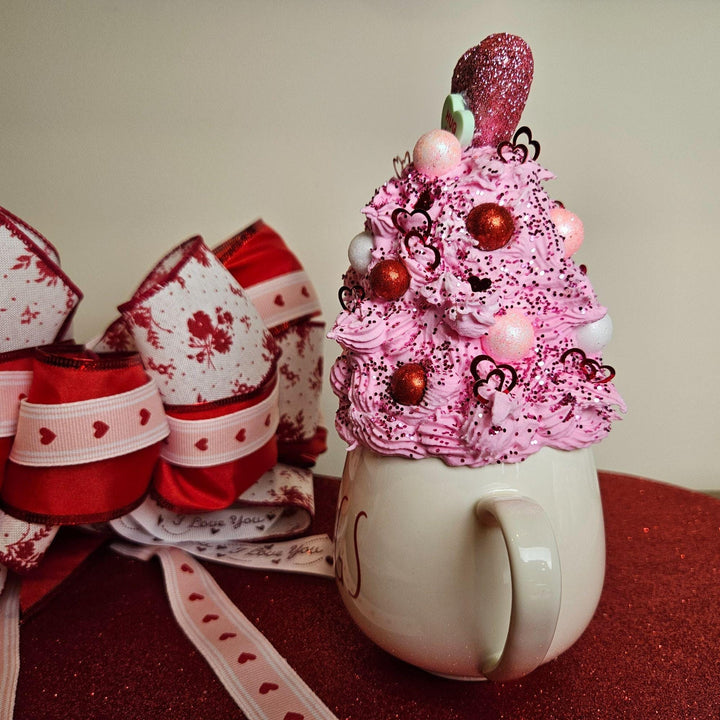 Decorative mug with pink whipped cream and candy on a red surface