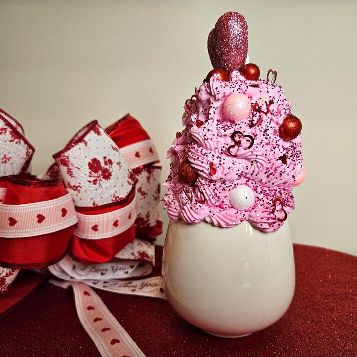 Decorative milkshake with pink whipped cream and red ornaments, surrounded by festive ribbons.